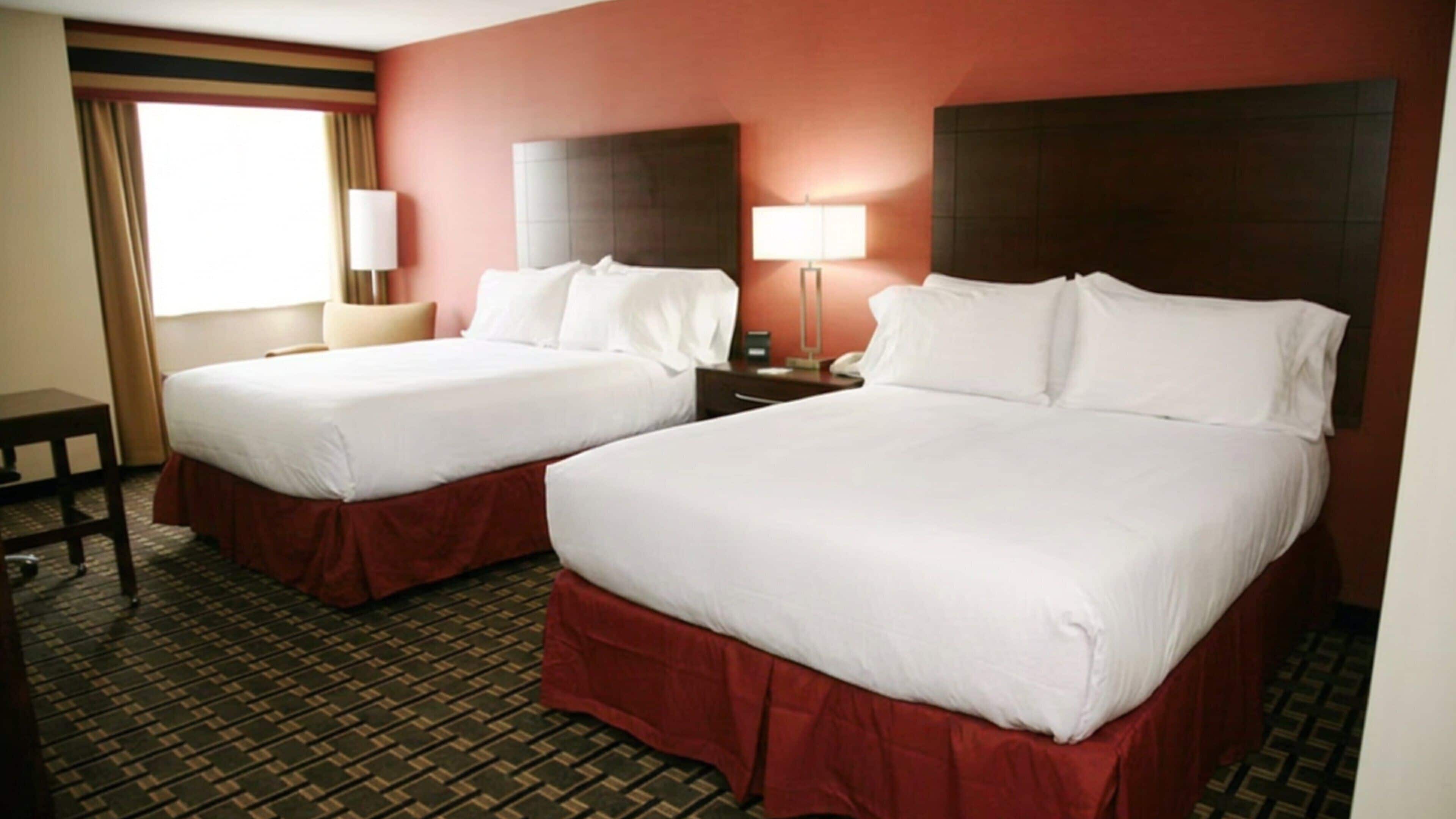 A hotel room with two beds, a desk, and a lamp.