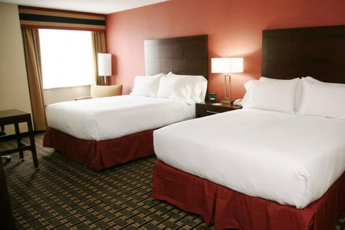 A hotel room with two beds, a desk, and a lamp.