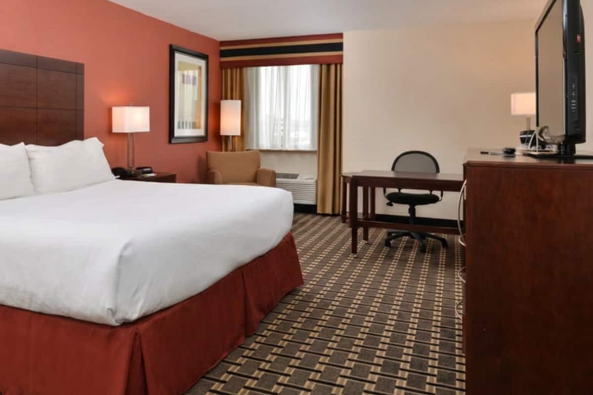 A hotel room with a large bed, a desk, a chair, a TV, and a window with curtains.