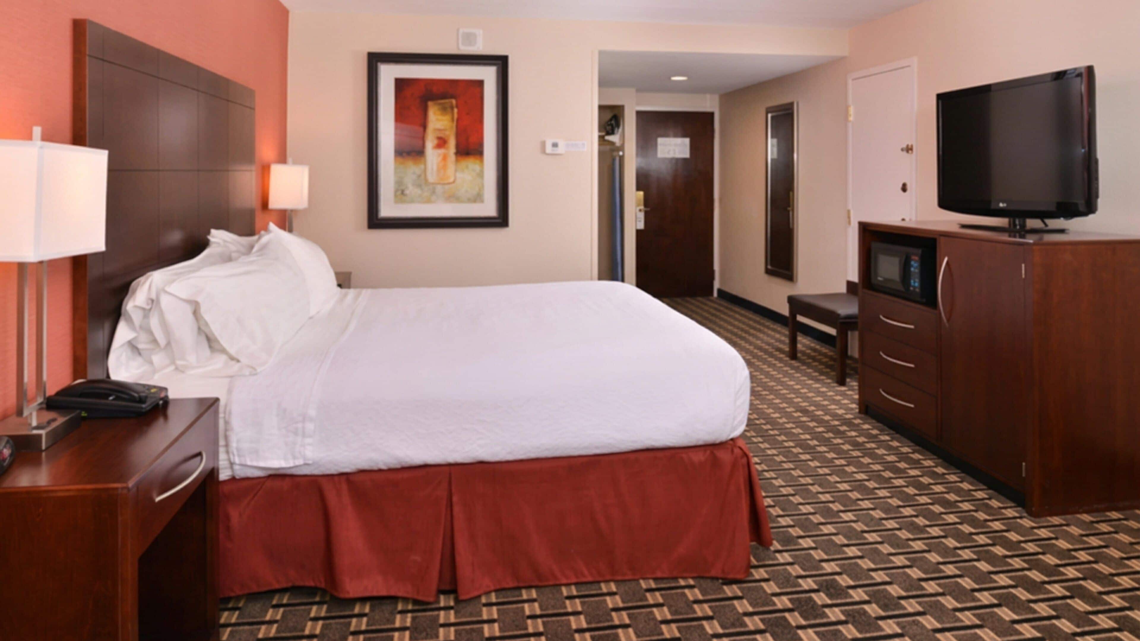 A hotel room with a bed, a desk with a telephone, a television, a wardrobe, and a framed picture on the wall.