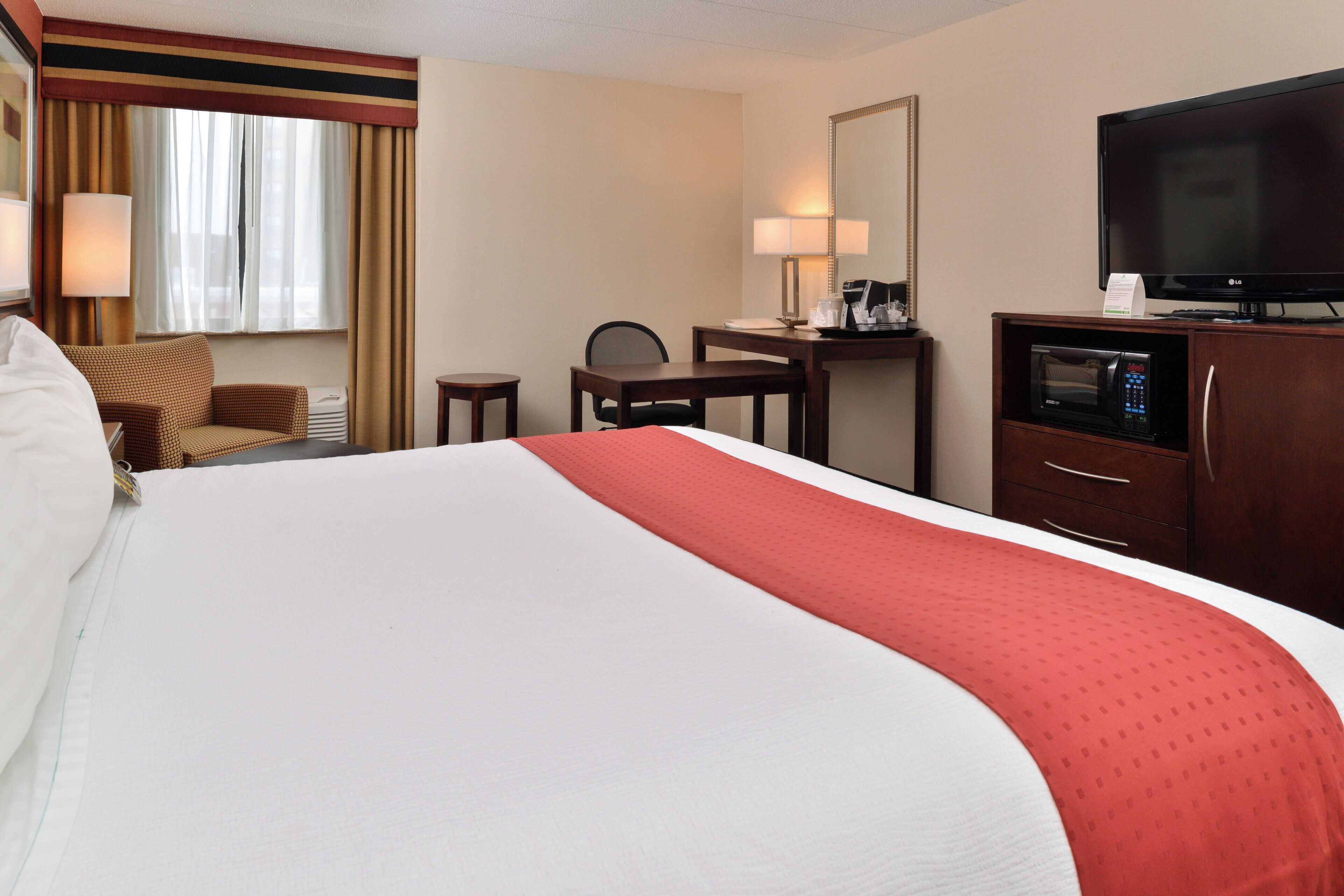 A hotel room with a large bed, a desk, a chair, a television, and a microwave.