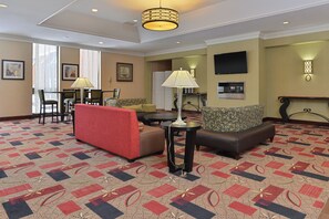 A hotel lobby with a red sofa, patterned armchairs, a coffee table, and a television on the wall. - Holiday Inn New London - Mystic Area by IHG (New London)
