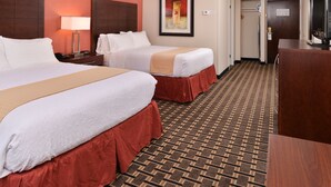 Habitación de hotel con dos camas, un escritorio, un televisor y una alfombra estampada.