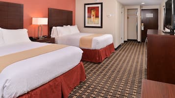 A hotel room with two beds, a desk, a TV, and a patterned carpet.