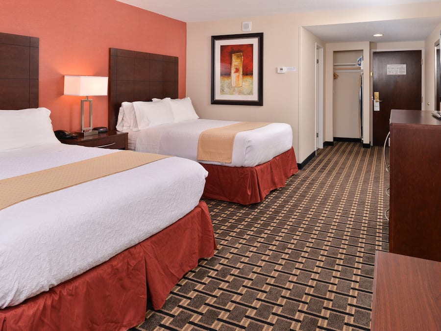 A hotel room with two beds, a desk, a TV, and a patterned carpet.
