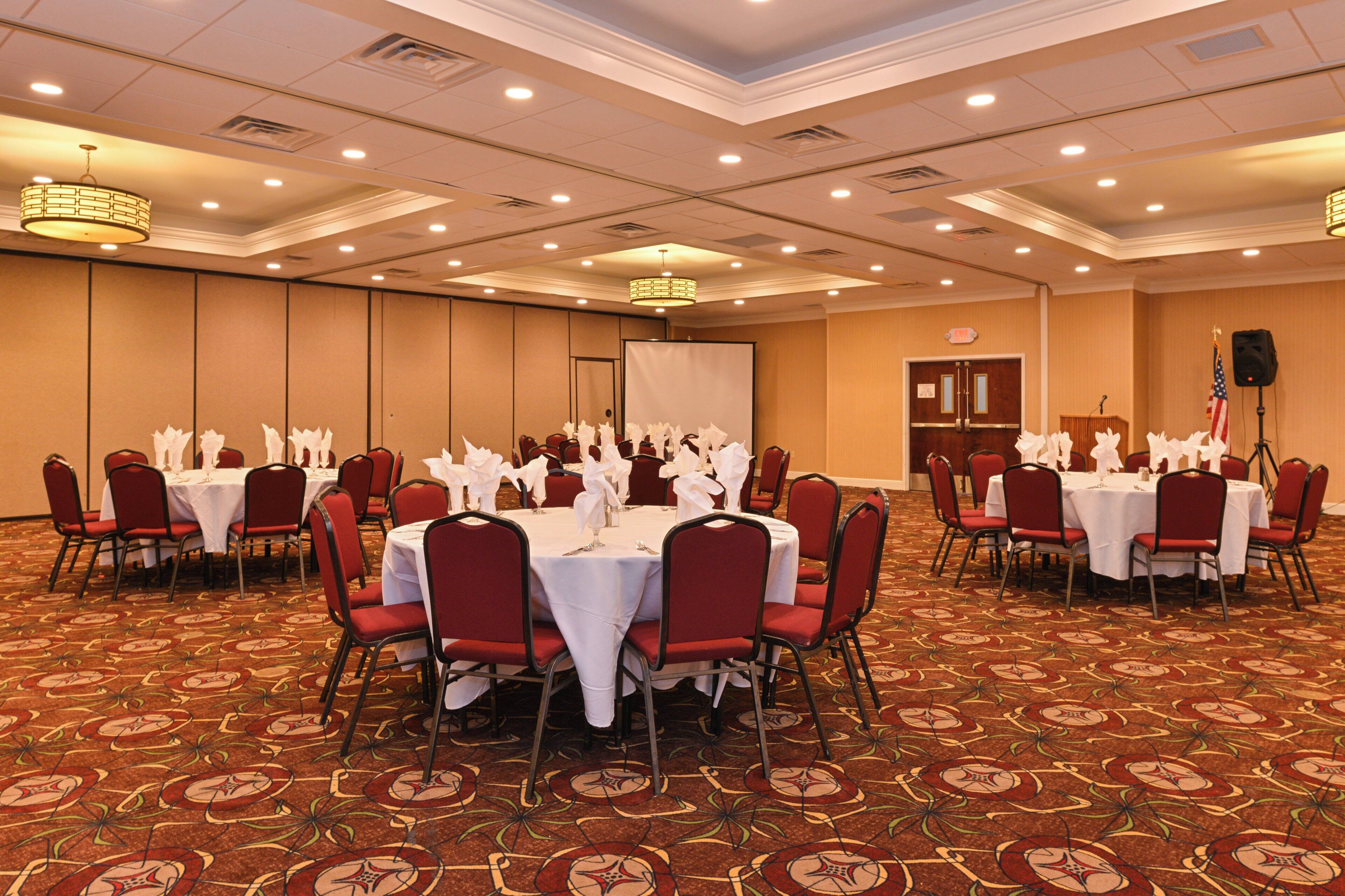 A conference room with round tables, red chairs, and white tablecloths.