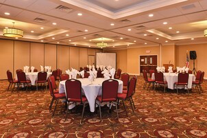 Un salón de conferencias con mesas redondas, sillas rojas y manteles blancos.
