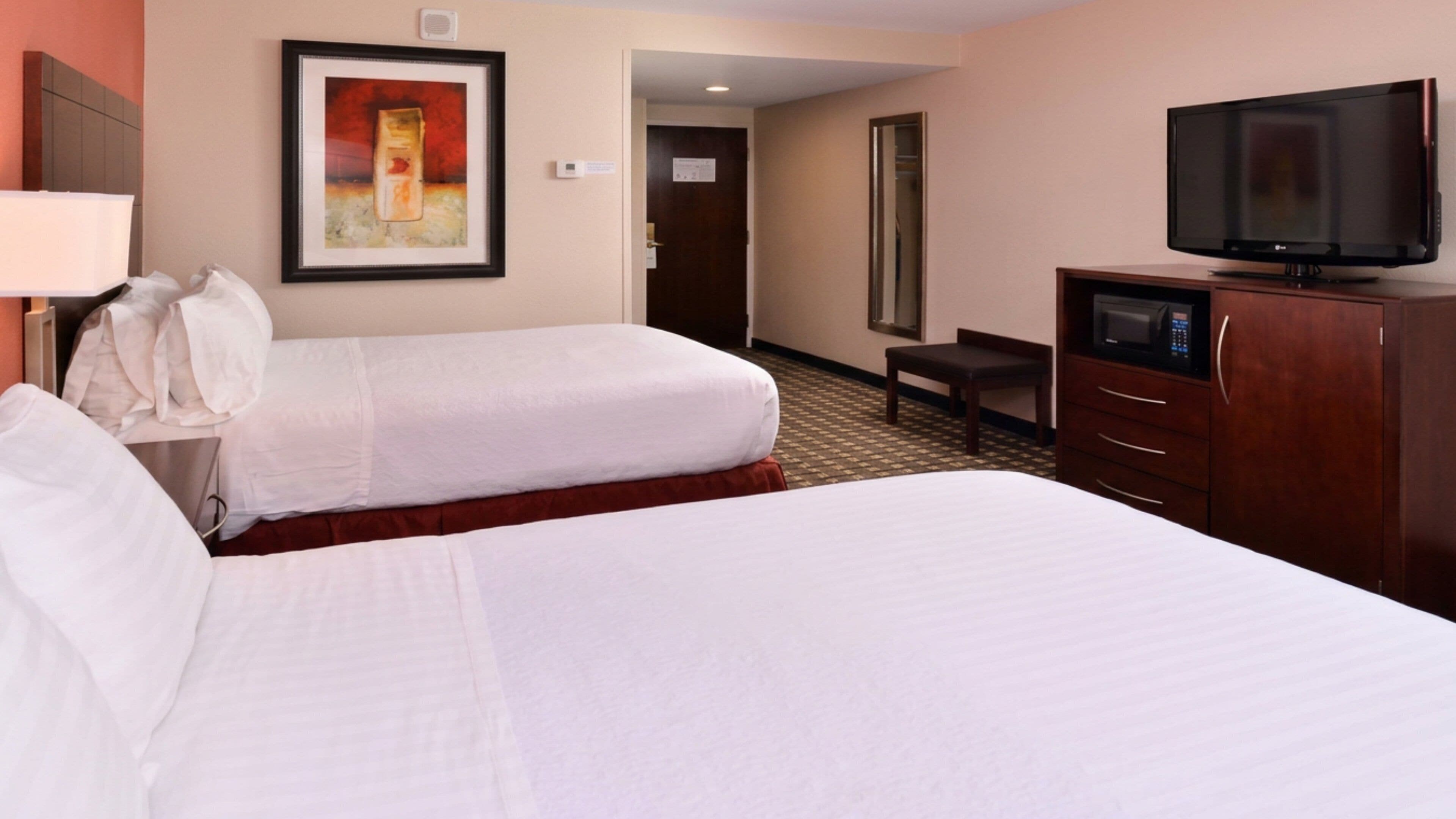 A hotel room with two beds, a television, a desk, and a painting on the wall.