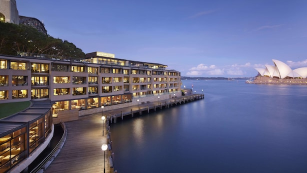 Un hotel frente al agua con varios pisos, un muelle y vistas de la Ópera de Sídney.