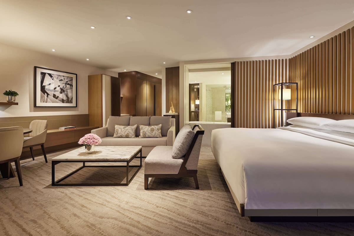 A modern hotel room with a large bed, a sofa, a desk, and a coffee table.