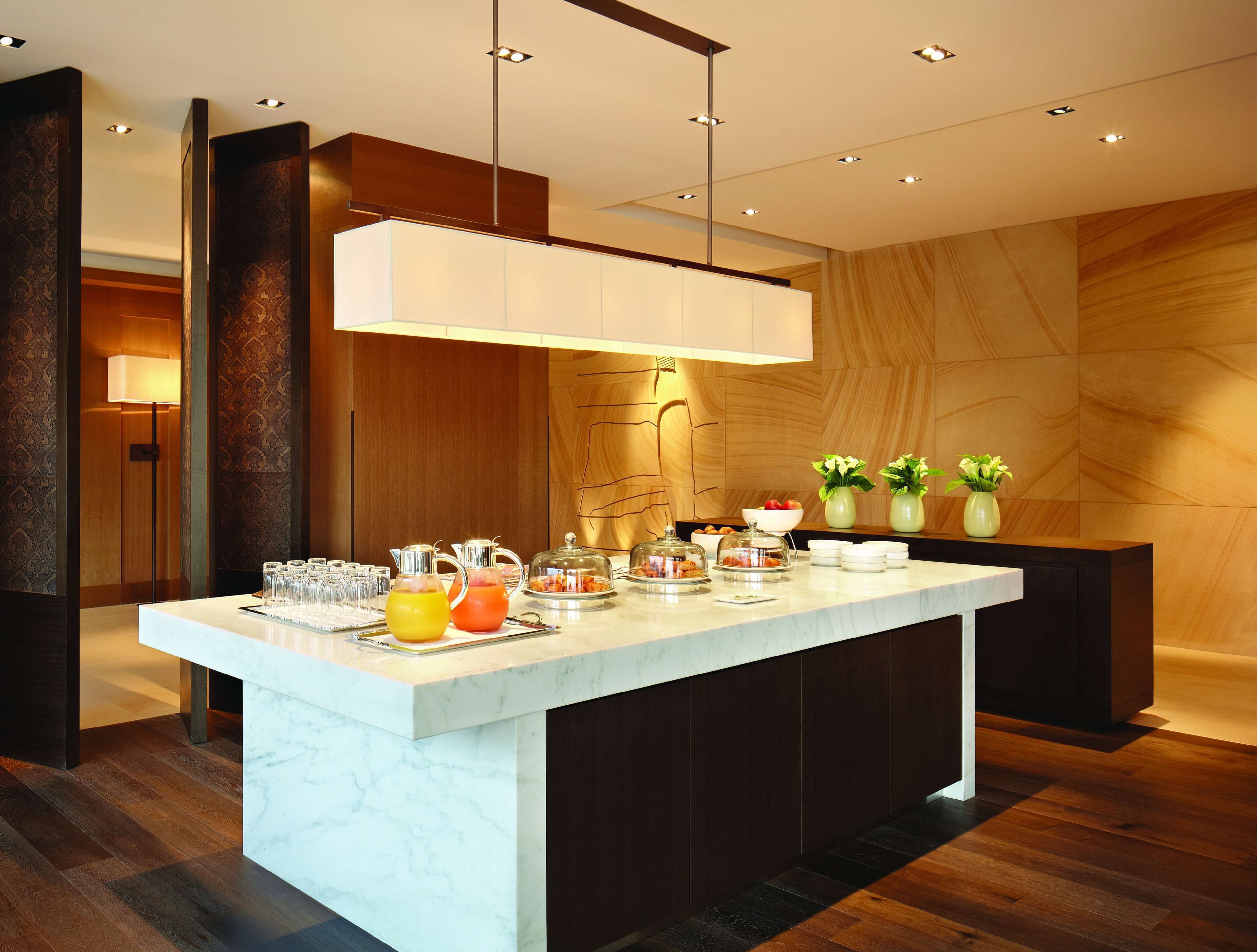 Una cocina moderna con encimera de mármol, lámpara colgante y pared de madera con diseño geométrico.