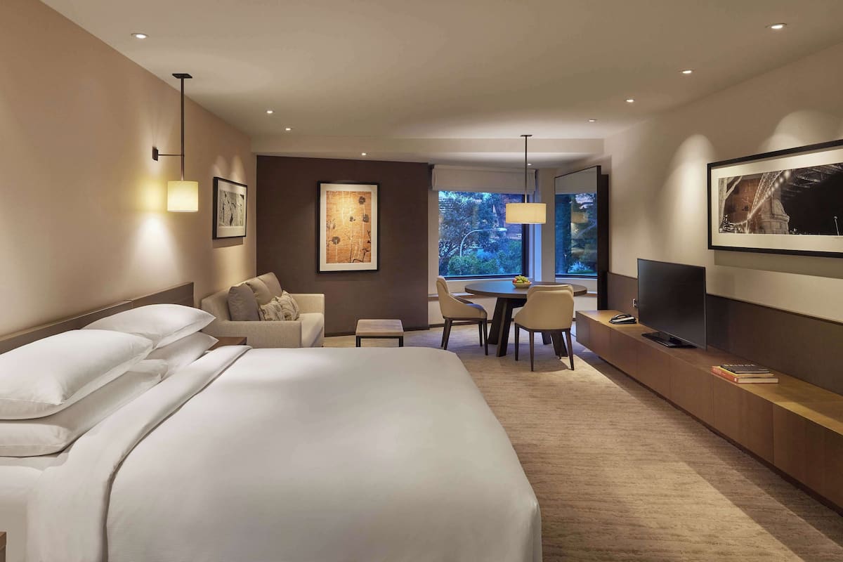 A hotel room with a large bed, a desk, a chair, a television, and artwork on the walls.