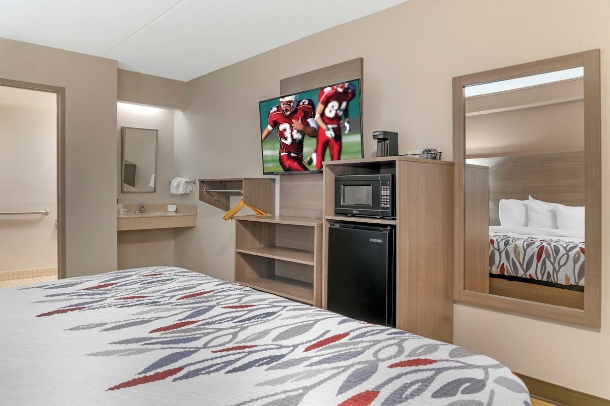 Habitación de hotel con cama, televisor, microondas, refrigerador, espejo y ventana con vista.