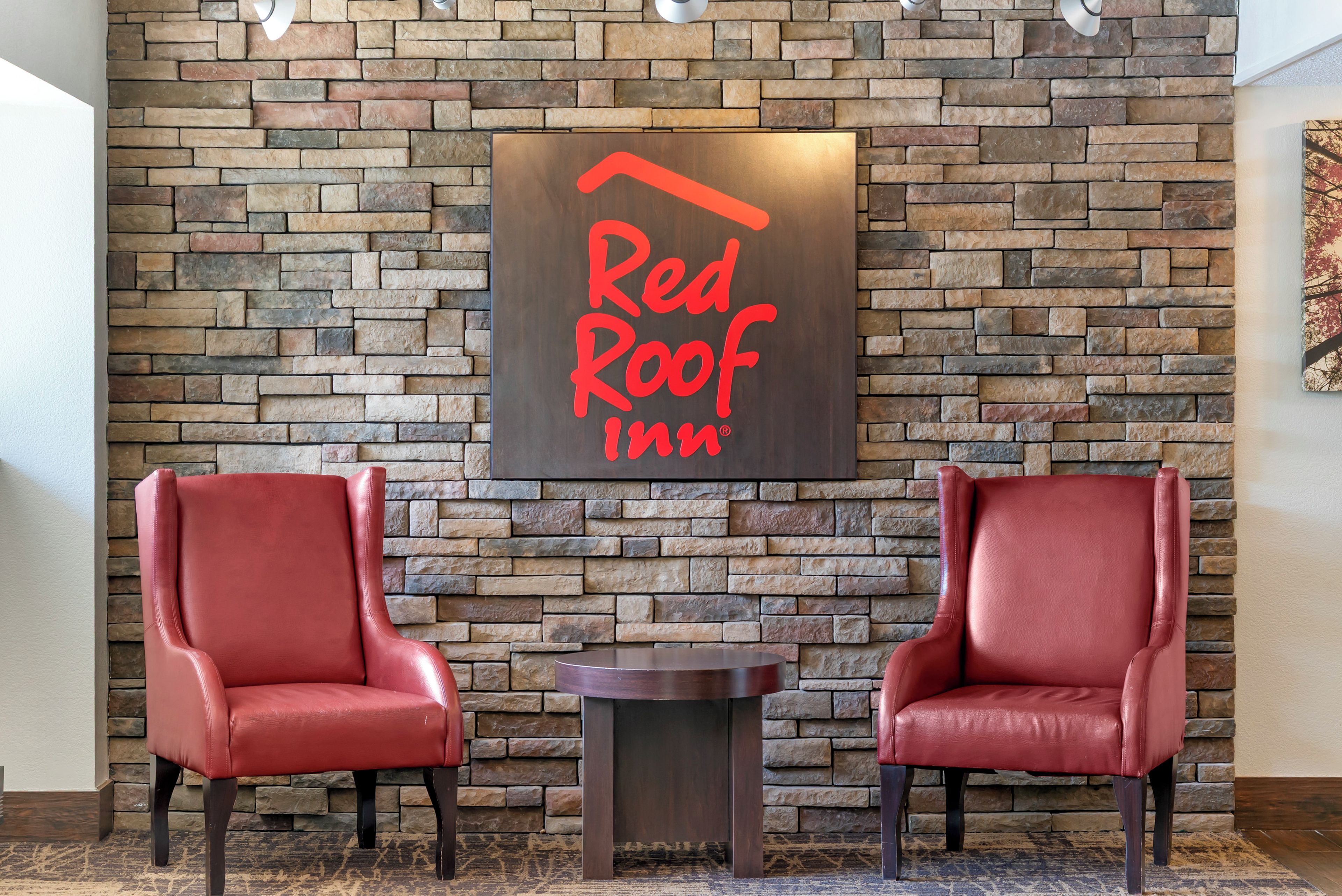 Et Red Roof Inn skilt på en stenvæg med to læderstole og et lille bord foran.