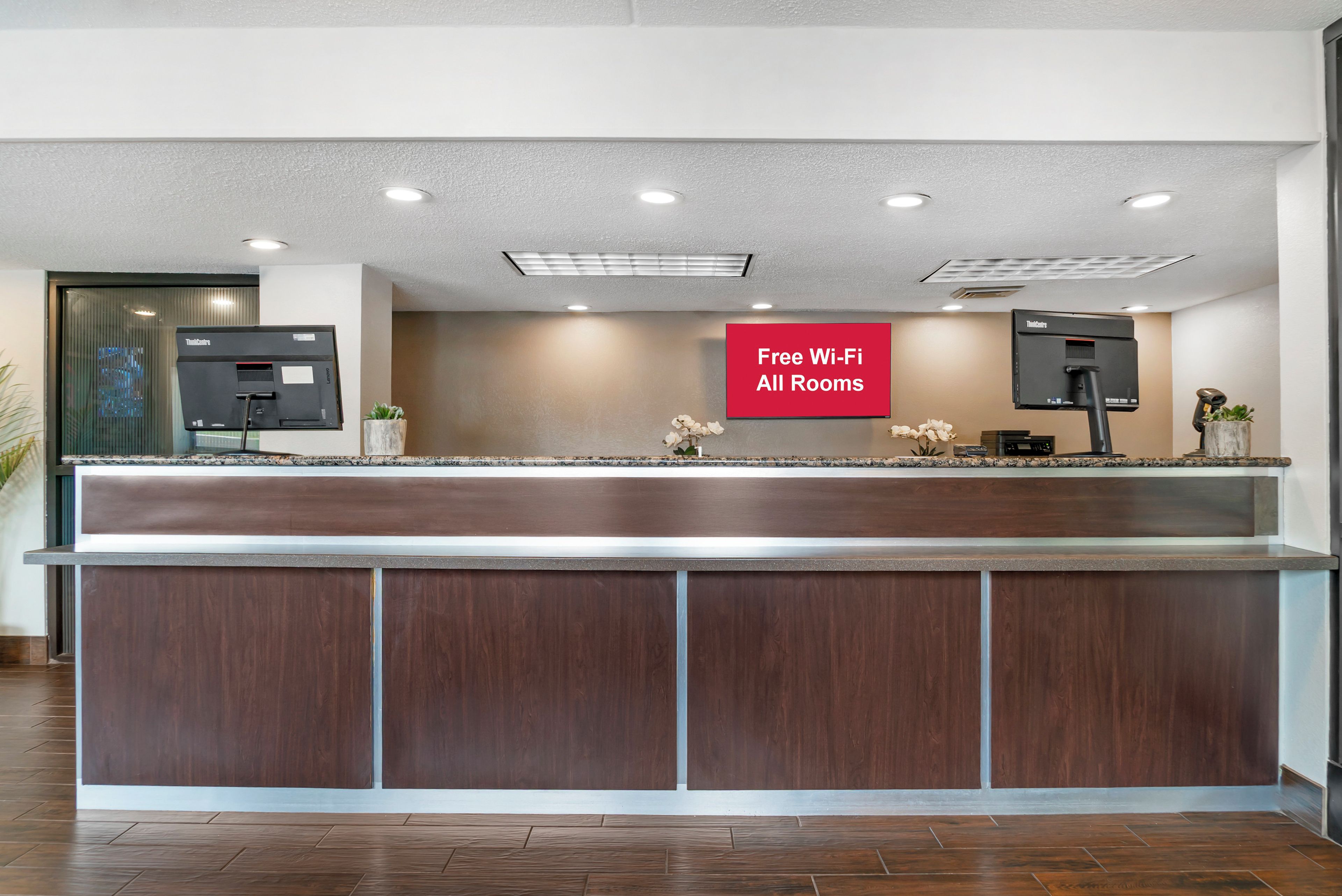 A reception desk with a 'Free Wi-Fi All Rooms' sign, a flat-screen TV, and a potted plant.