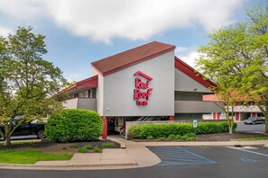 A Red Roof Inn with a modern architectural design, a parking lot, and surrounding greenery. - Red Roof Inn Detroit-Rochester Hills/Auburn Hills (Rochester)