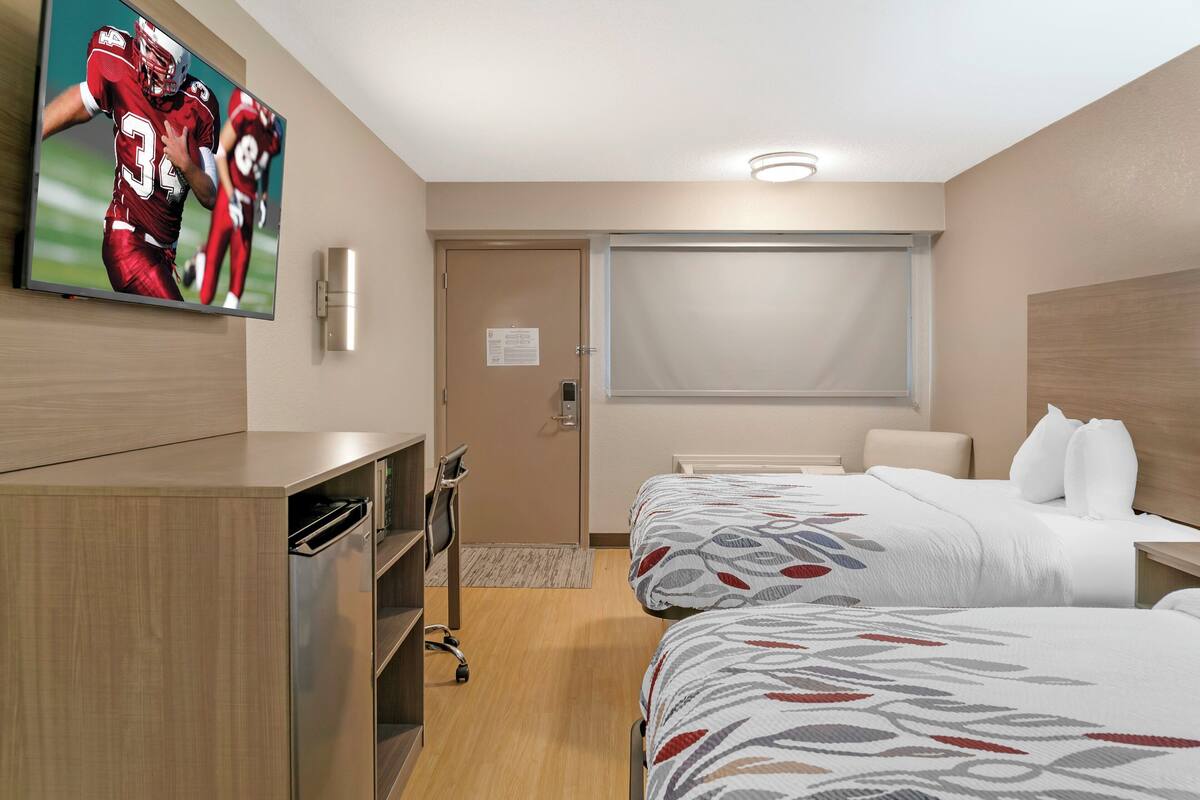 A hotel room with two beds, a TV on the wall, a desk, and a wardrobe.