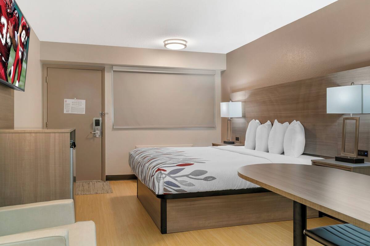 A hotel room with a bed, bedside tables, a desk, a chair, a TV, and a door.