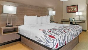 Una habitación de hotel con una cama grande, dos mesitas de noche con lámparas, un escritorio con silla y un cuadro enmarcado en la pared.