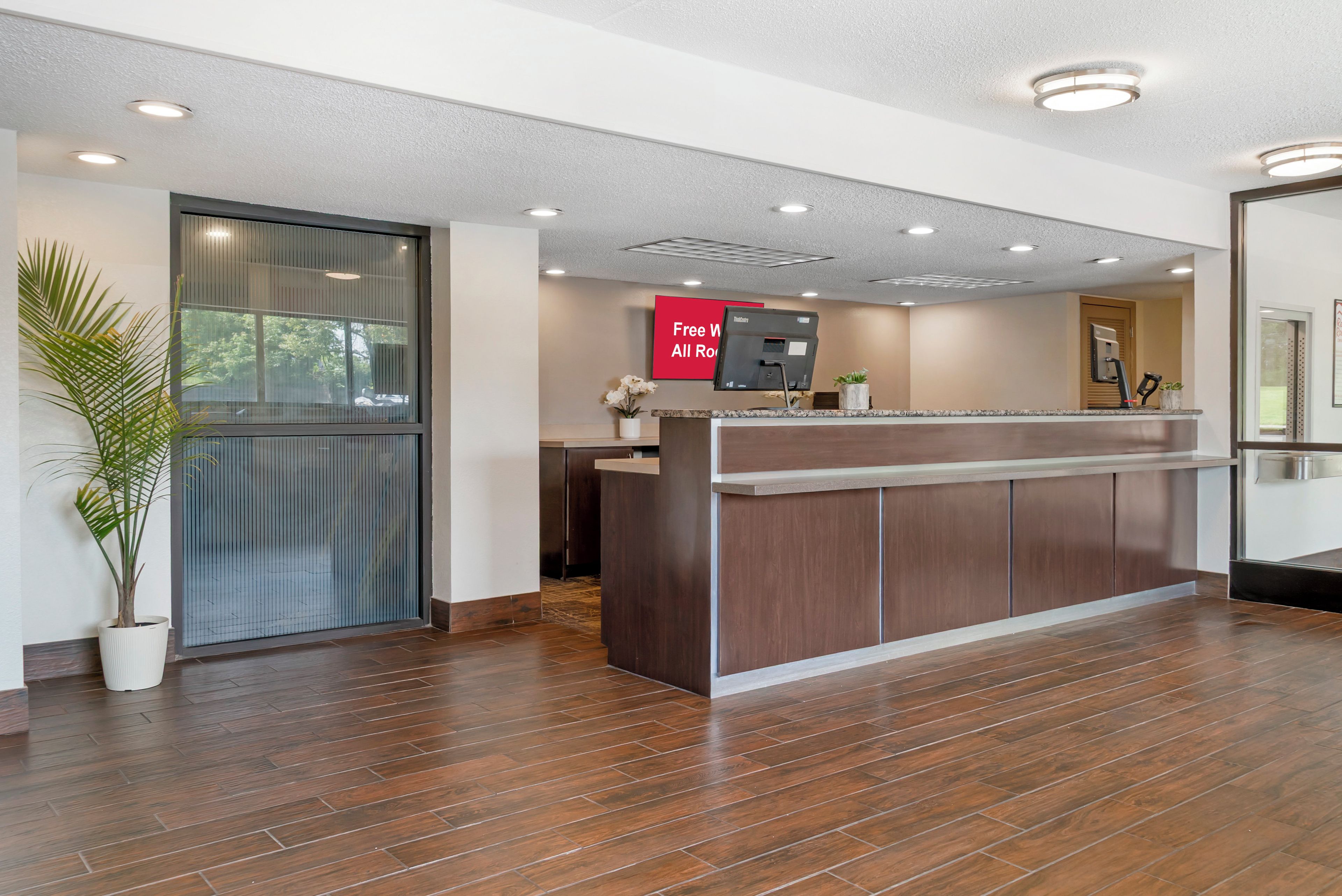 A reception desk with a digital screen, a potted plant, and a sign offering free Wi-Fi.