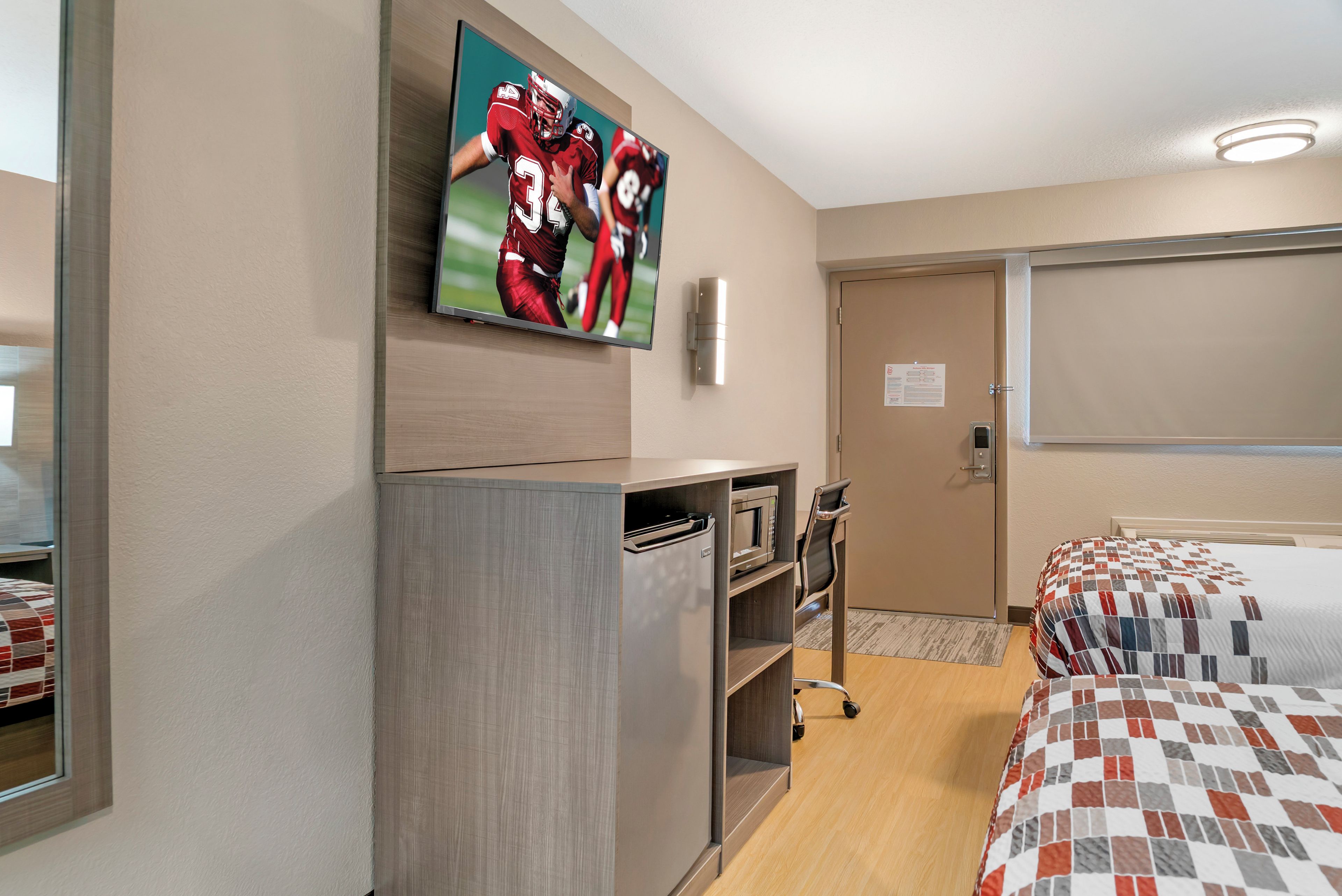 Ein Hotelzimmer mit einem Bett, einem an der Wand befestigten Fernseher, einer Mikrowelle und einer Tür mit einem Schild.
