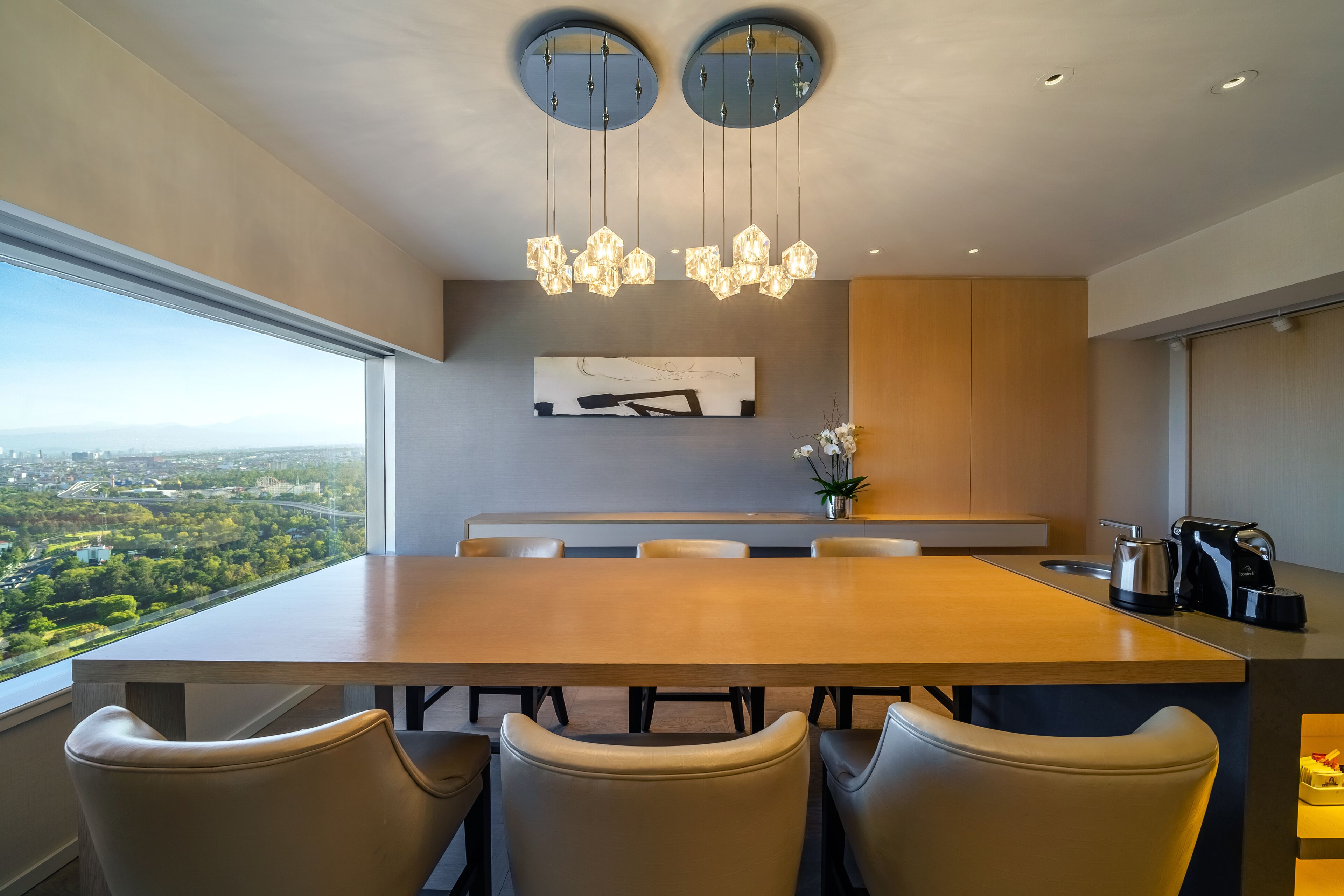 Un espace repas moderne avec une grande table, quatre chaises et une vue sur la ville grâce à de larges fenêtres.