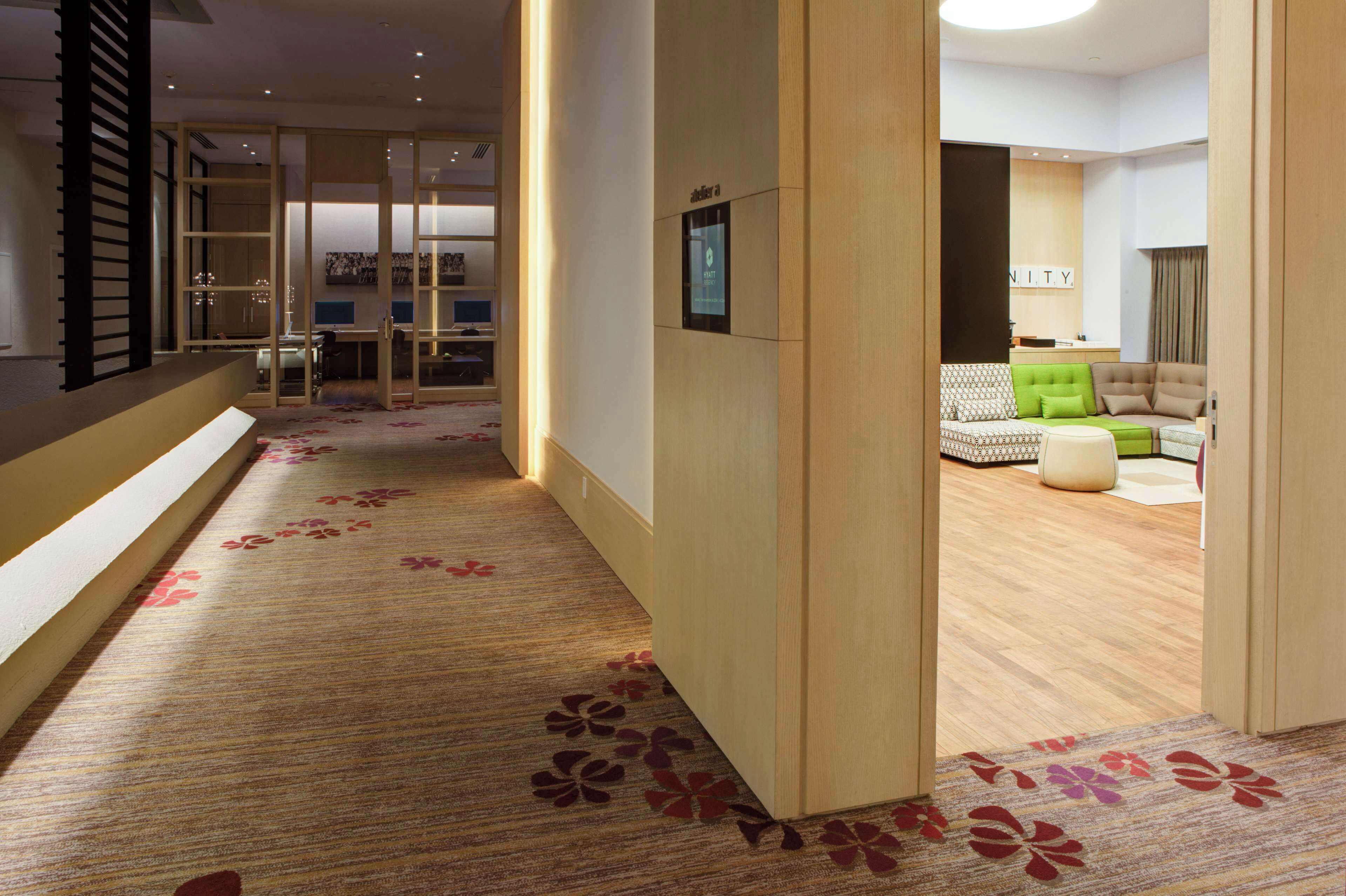 Un vestíbulo de hotel con piso alfombrado, un mostrador de recepción y un área de estar con sofá y reposapiés.