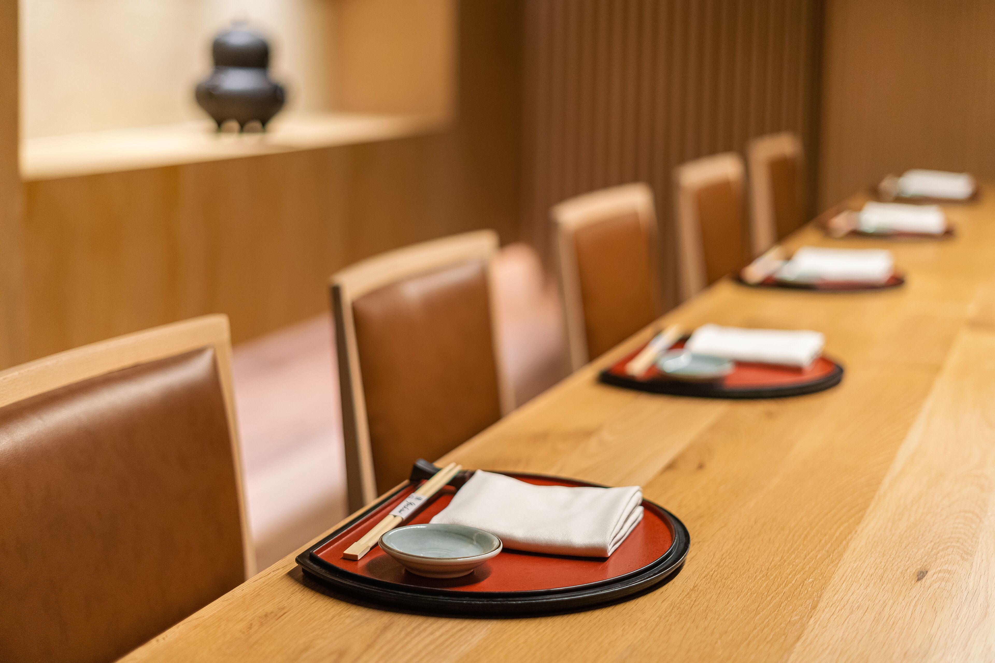 A dining area with a long wooden table set with red placemats, white napkins, and a small bowl.