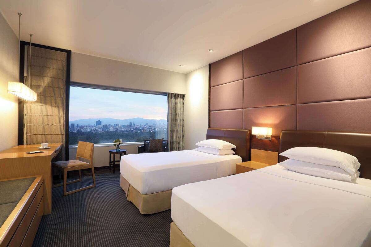 Une chambre d’hôtel avec deux lits, un bureau, une chaise et une vue sur le paysage urbain.