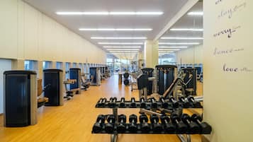 Un gimnasio con equipo de ejercicio, un muro de espejos con frases motivacionales y piso de madera.