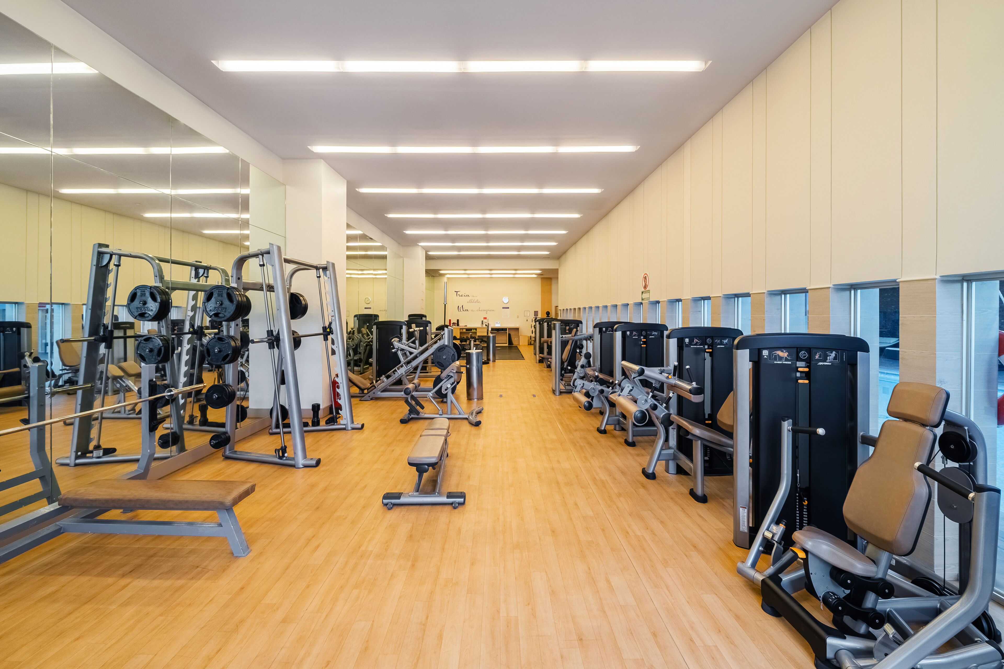 Un gimnasio con diversas máquinas de ejercicio, piso de madera y espejos en las paredes.