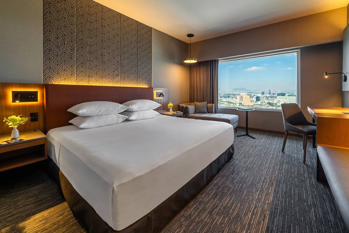 Une chambre d’hôtel avec un grand lit, un bureau, une chaise, une petite table et une vue sur la ville.