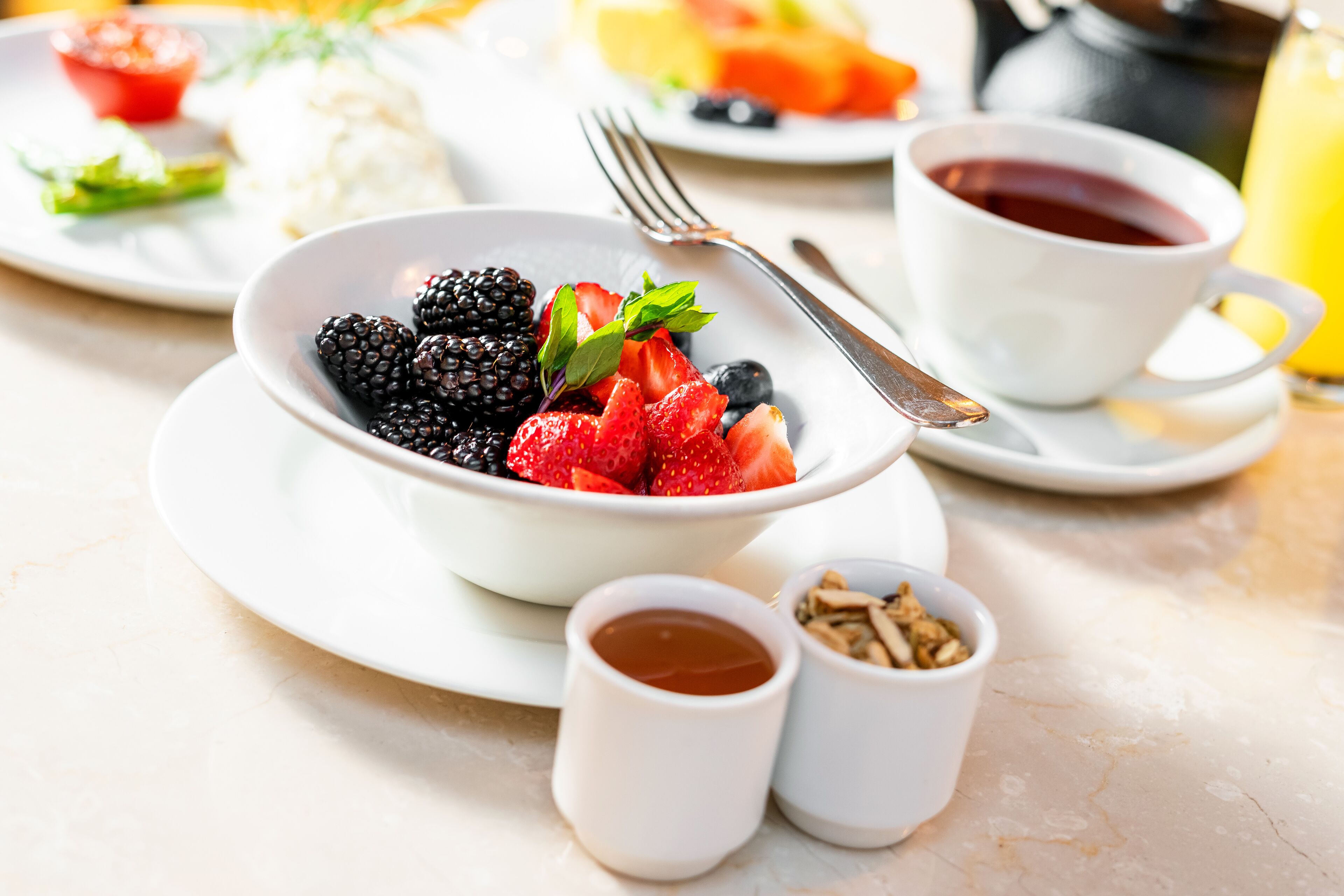Desayuno con un tazón de frutos rojos, una taza de té y un vaso de zumo de naranja.