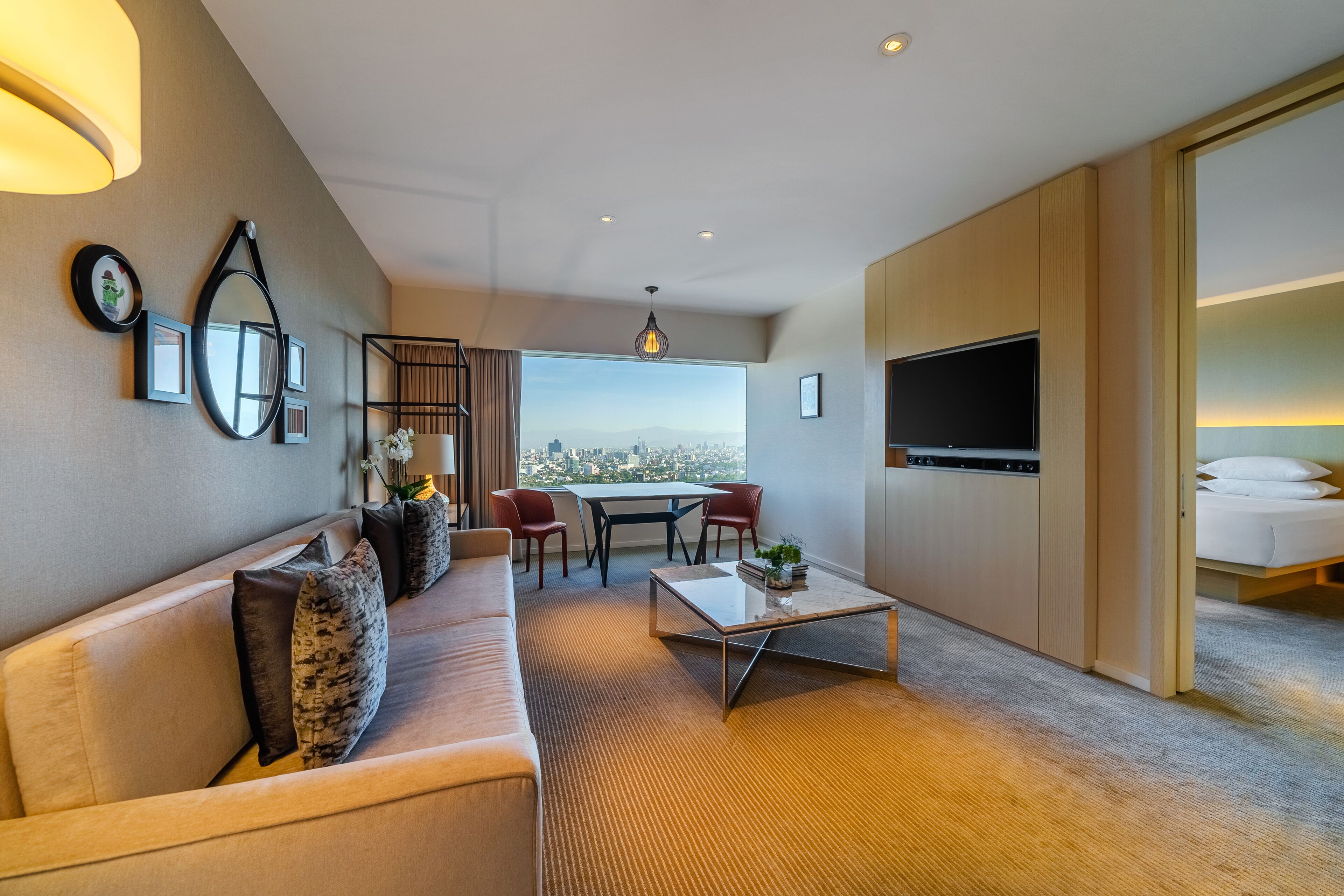 Una habitación de hotel moderna con sofá, mesa de centro, televisor y un ventanal con vistas a la ciudad.