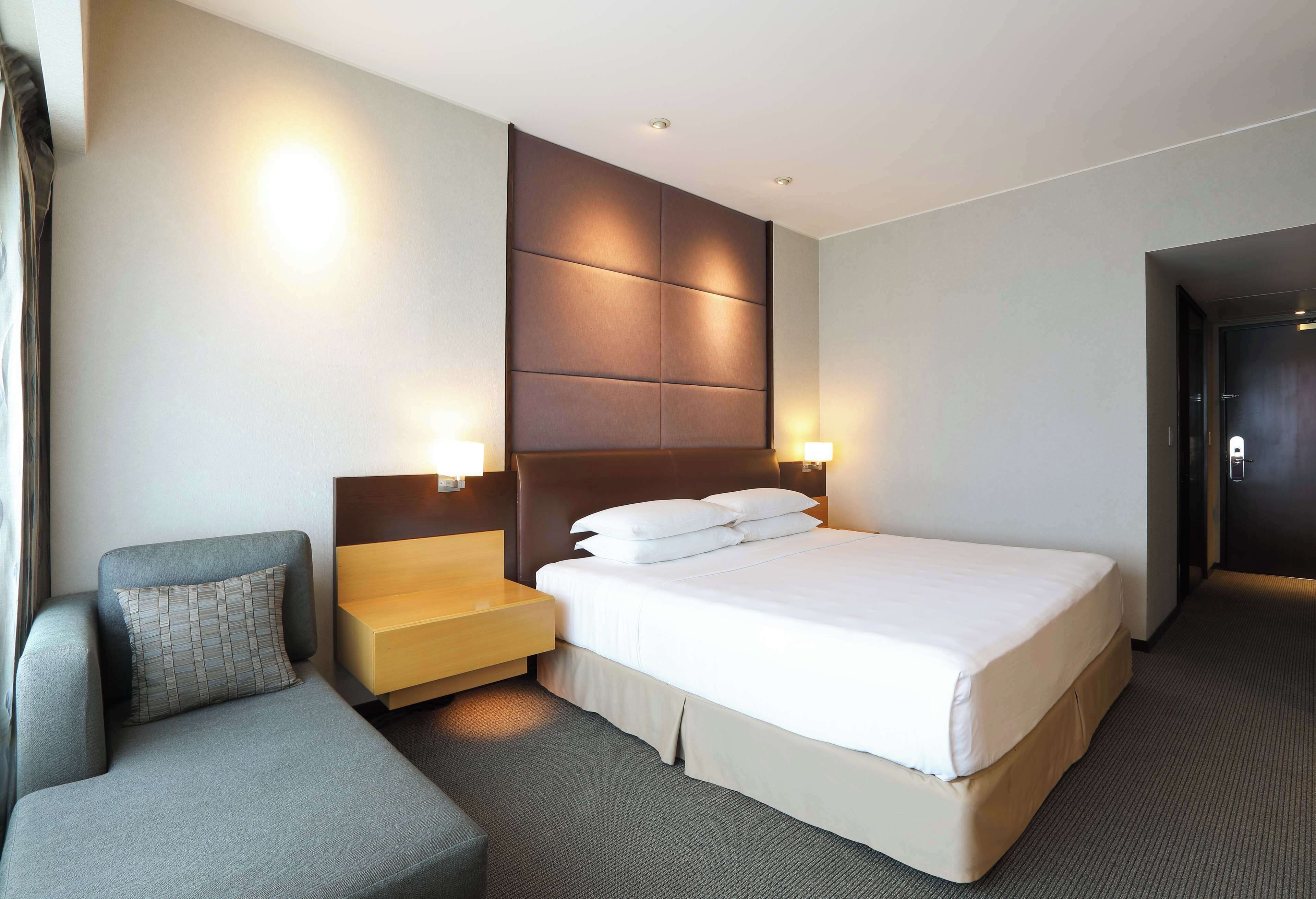 A modern hotel room with a large bed, a sofa, a nightstand, and two wall-mounted lamps.