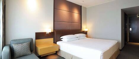 A modern hotel room with a large bed, a sofa, a nightstand, and two wall-mounted lamps.