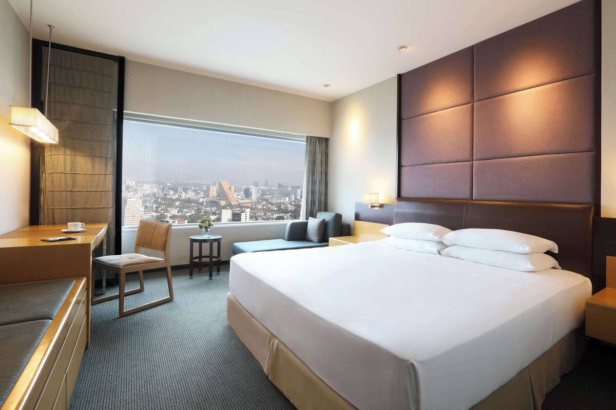 Une chambre d’hôtel avec un grand lit, un bureau, une chaise, une petite table et une vue sur la ville.