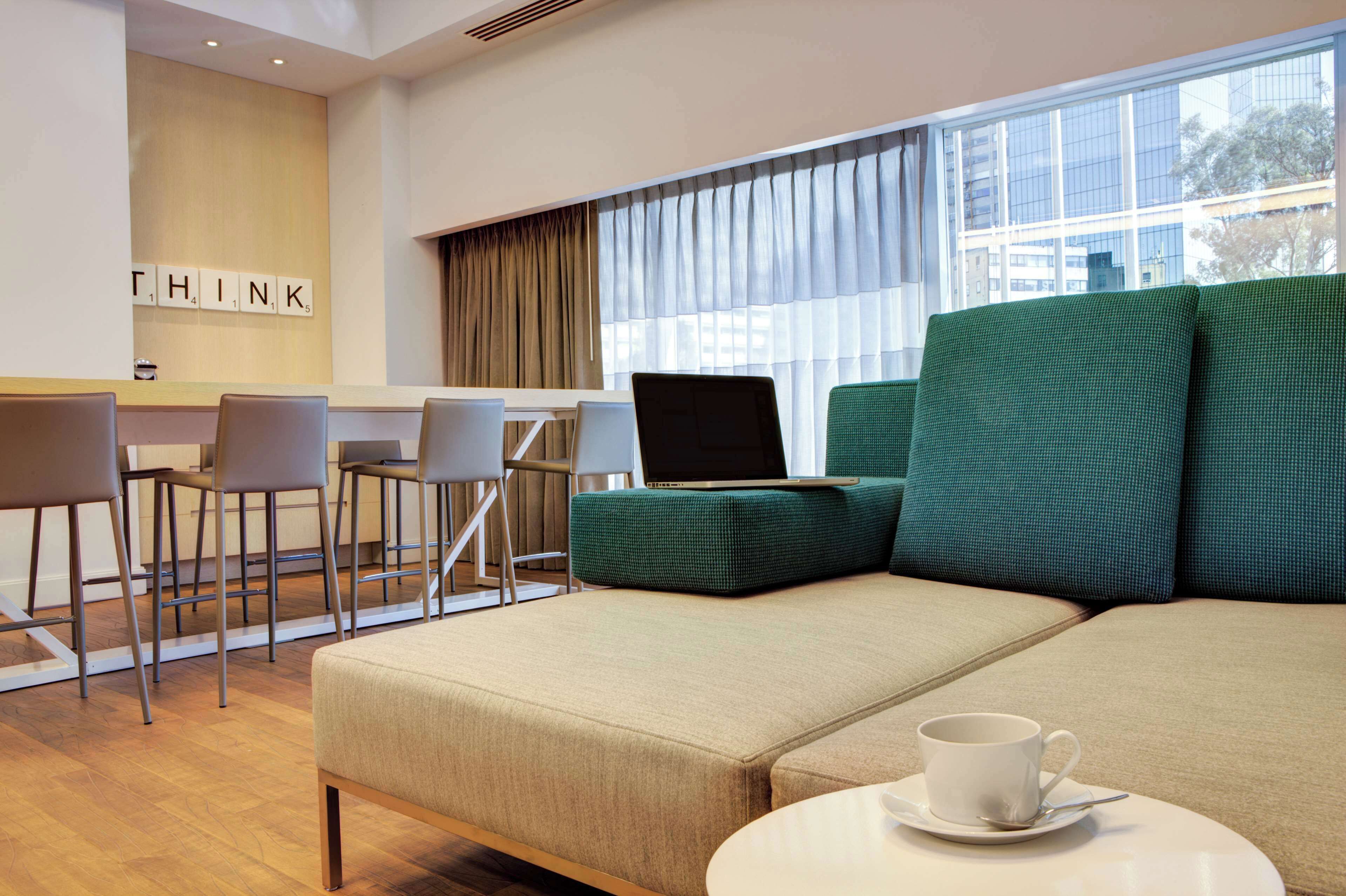 A modern lounge area with a sofa, chairs, a laptop, and a cup on a table.