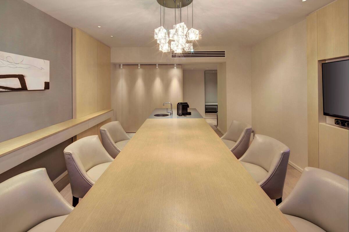 Une salle de conférence avec une longue table, six chaises, une machine à café et un téléviseur fixé au mur.