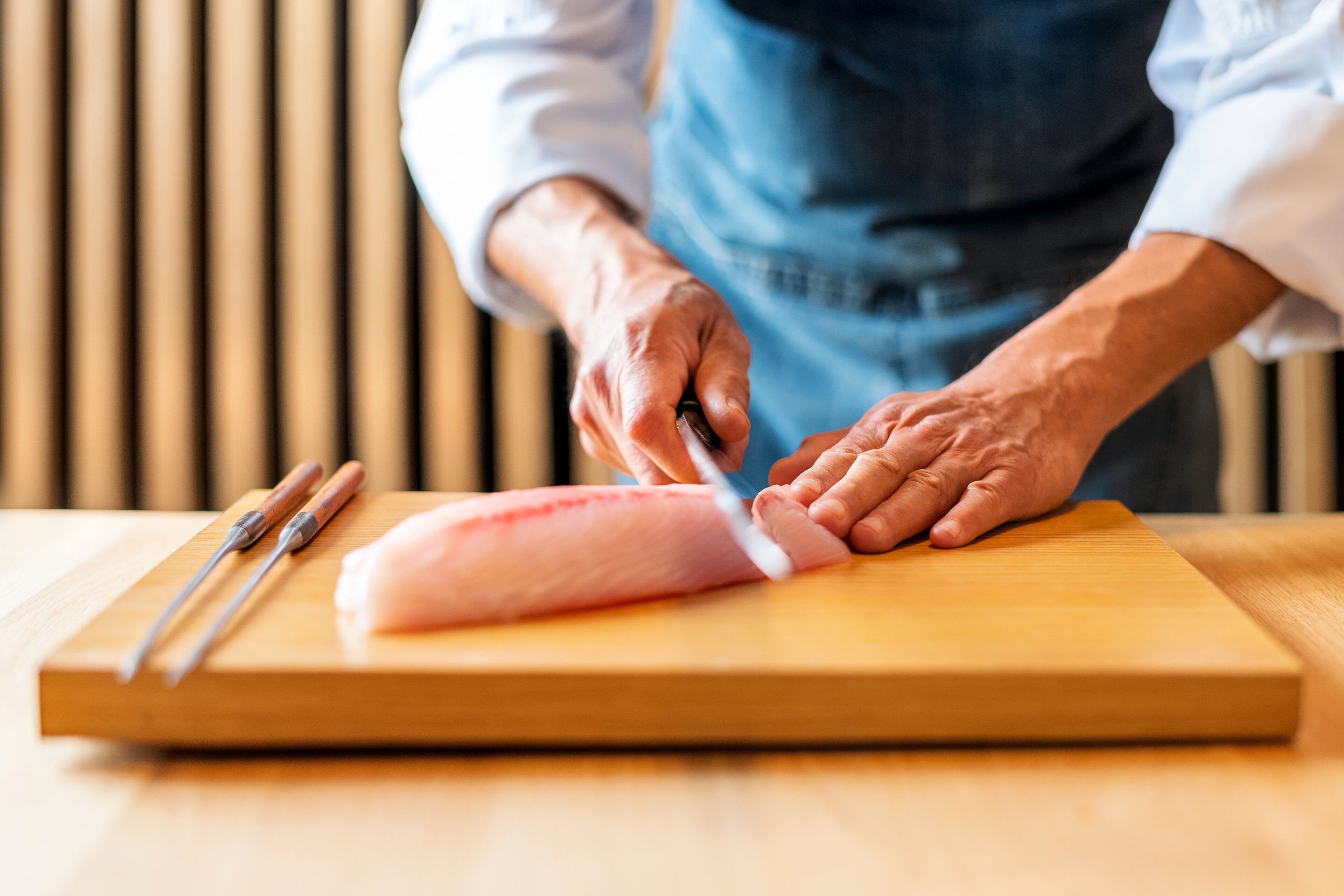 A person slicing a piece of meat on a wooden cutting board.
