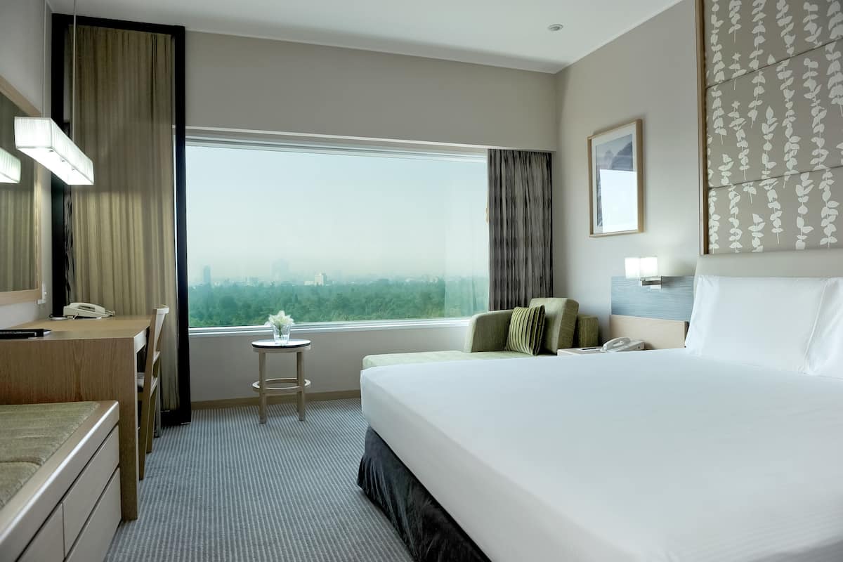 Une chambre d’hôtel avec un grand lit, un bureau, une chaise, une petite table, un téléphone et une fenêtre donnant sur la ville.