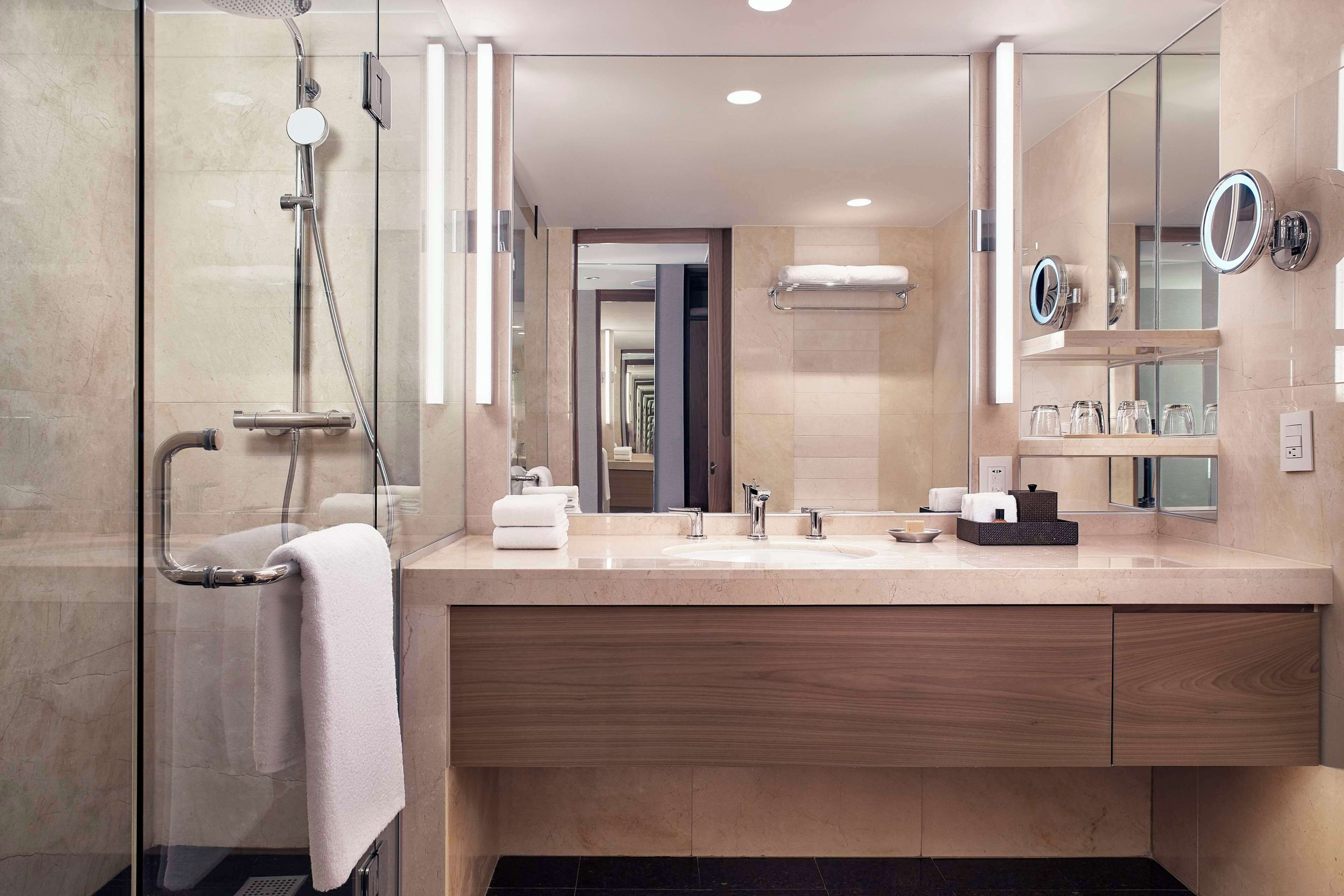 A modern bathroom with a glass-enclosed shower, a large mirror, and a vanity with a sink and towel rack.