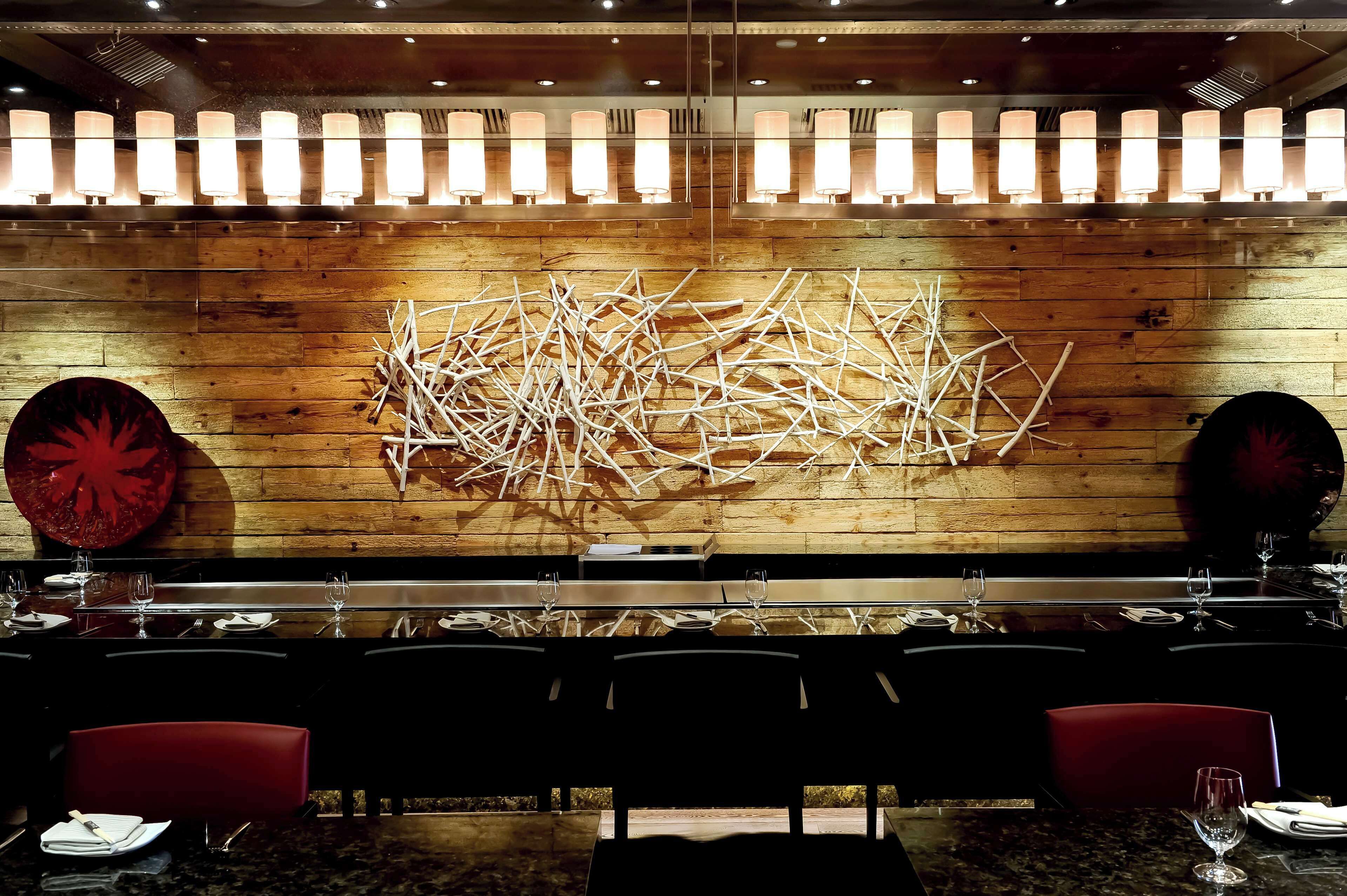 Un restaurant aux murs en bois, agrémenté de luminaires suspendus et orné d’une œuvre d’art moderne.