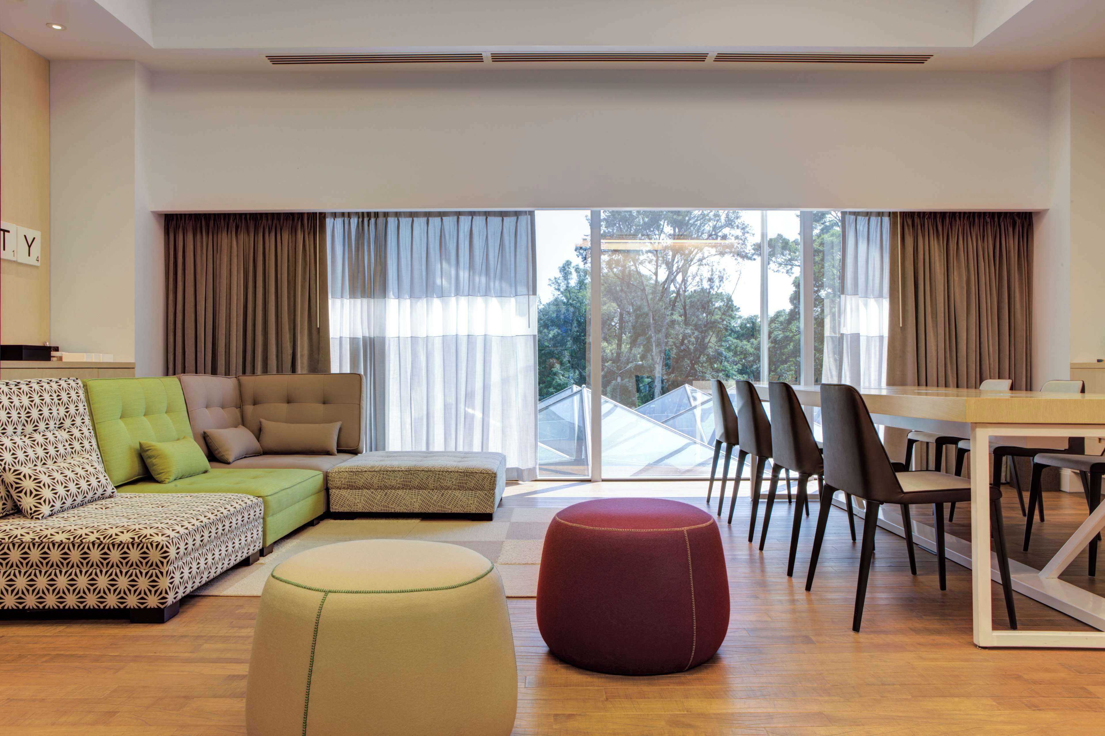 Una sala de estar moderna con un sofá modular, otomanas, una mesa de comedor con sillas y ventanas grandes con cortinas.