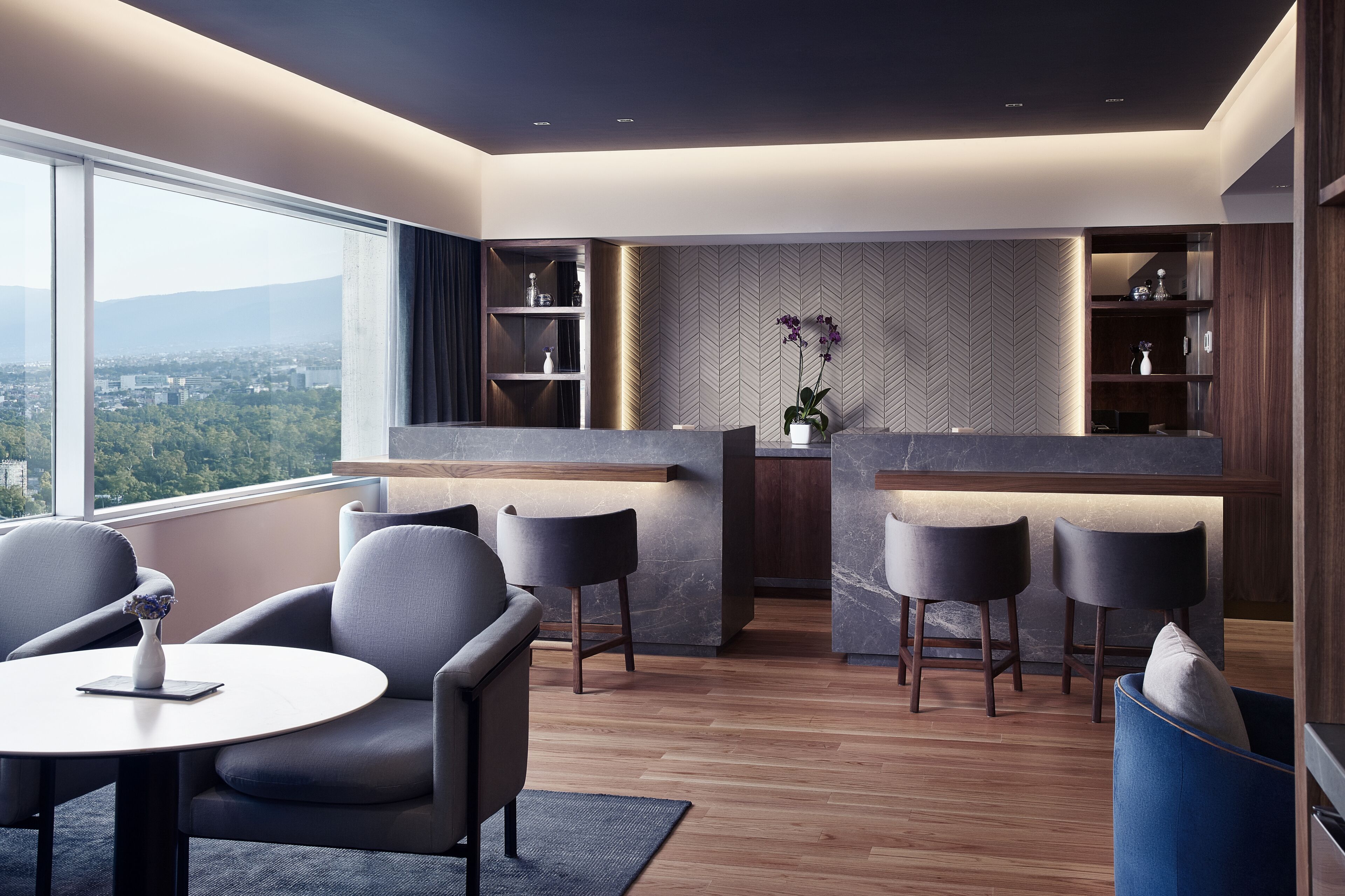 Una sala de estar moderna con zona de cocina, ventanas amplias y vista a la ciudad.