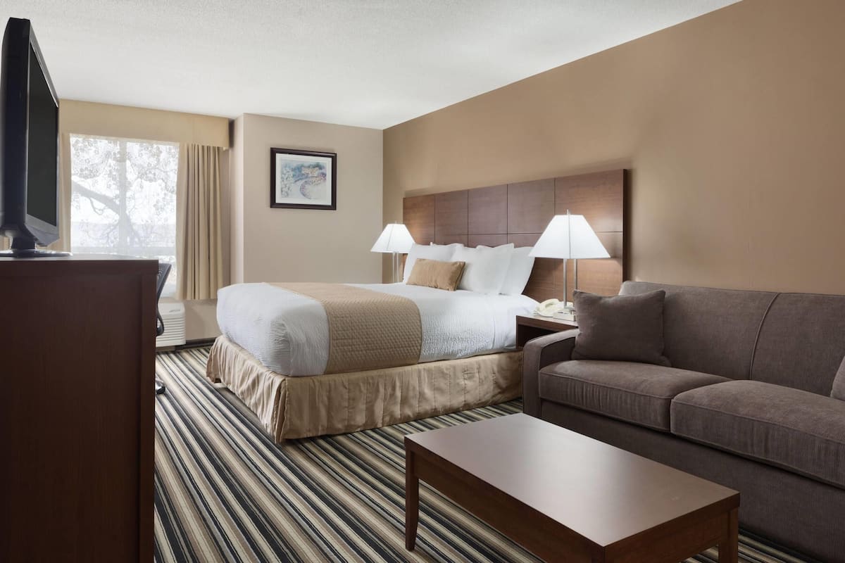 A hotel room with a bed, a sofa, a coffee table, a TV, and a window with curtains.