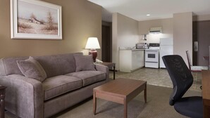 A living room with a sofa, a coffee table, a painting, a lamp, and a kitchen in the background. - Days Inn by Wyndham Dalhousie (Dalhousie)