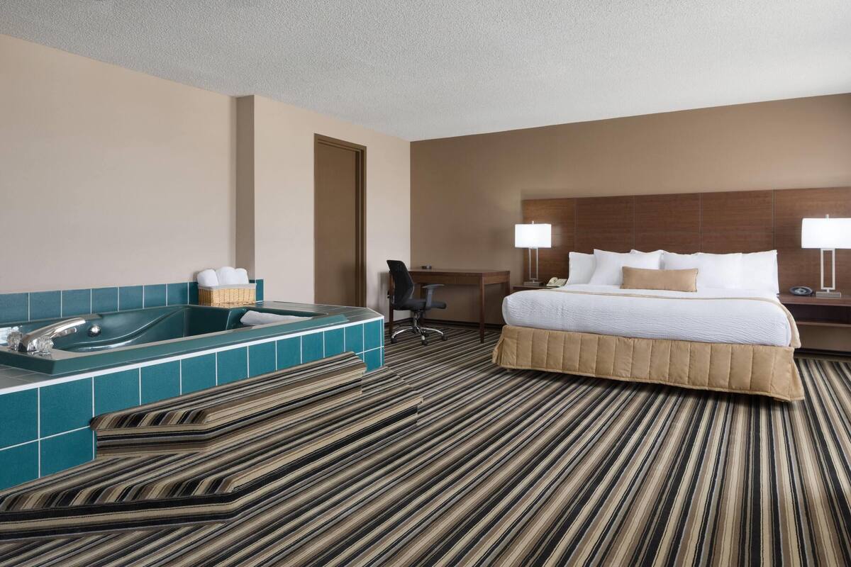 A hotel room with a large bed, a bathtub, a desk, and a chair.