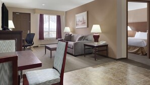A hotel room with a sofa, a dining table, a chair, a bedside table with a lamp, and a bed. - Days Inn by Wyndham Dalhousie (Dalhousie)