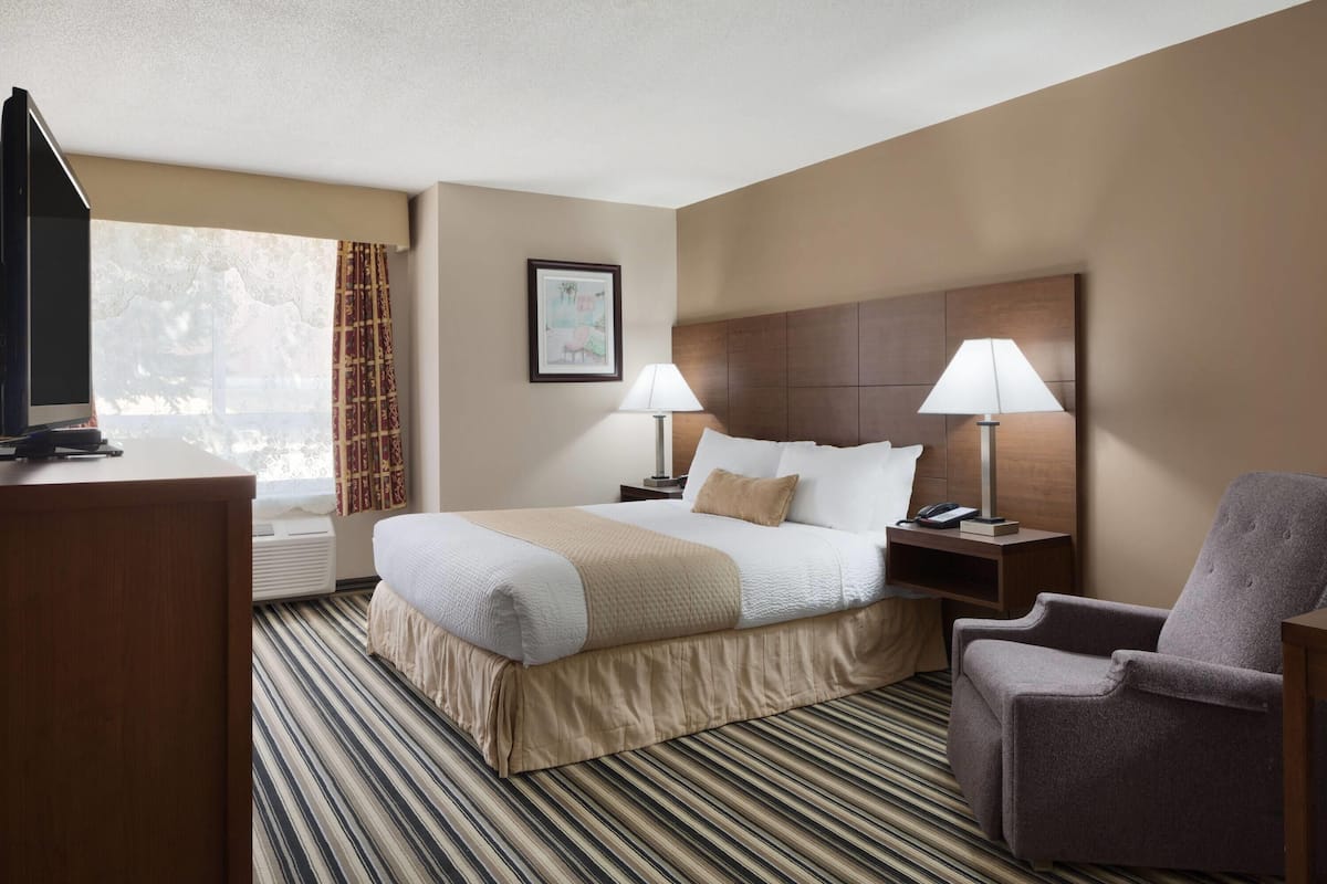 A hotel room with a large bed, two bedside lamps, a TV, a chair, and a window with curtains.